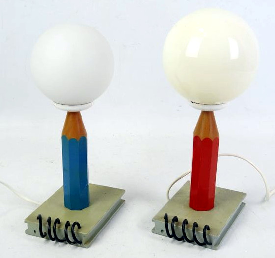 Table lamps with a spiral-bound notebook as a base, a pencil as the holder, and then a round globe on top.